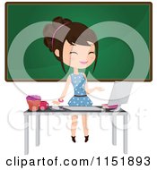 Female Teacher At A Desk With A Computer By A Chalkboard