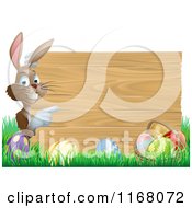 Poster, Art Print Of Brown Bunny Pointing To A Wooden Sign Over Easter Eggs In Grass