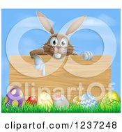 Poster, Art Print Of Brown Bunny Pointing Down To A Wood Sign With Grass And Easter Eggs Against Blue Sky