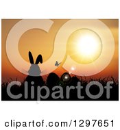 Poster, Art Print Of Silhouetted Easter Bunny With Eggs A Butterfly And Grass Against An Orange Sunset