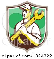Clipart Of A Retro Male Mechanic Holding A Wrench And Emerging From A Taupe White And Green Shield Royalty Free Vector Illustration