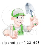 Young Brunette White Male Gardener In Green Holding Up A Shovel And Giving A Thumb Up