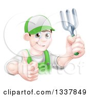 Poster, Art Print Of Happy Young Brunette White Male Gardener In Green Holding Up A Garden Fork And Thumb
