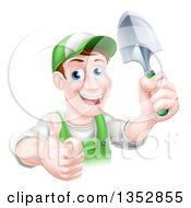 Happy Middle Aged Brunette White Male Gardener In Green Giving A Thumb Up And Holding A Shovel