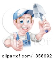 Happy Young Brunette White Male Gardener In Blue Giving A Thumb Up And Holding A Shovel