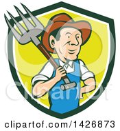 Retro Cartoon Male Farmer Or Worker Holding A Pitchfork Over His Shoulder Emerging From A Green White And Yellow Shield