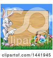 Poster, Art Print Of Cartoon Happy White Easter Bunny Rabbit Pointing Around A Wood Sign With A Basket And Eggs Against Sky
