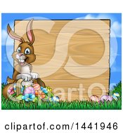 Poster, Art Print Of Cartoon Happy Brown Easter Bunny Rabbit Holding A Basket In Front A Wood Sign Against Sky