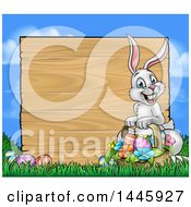 Poster, Art Print Of Happy Easter Bunny With A Basket Of Eggs And Flowers In The Grass With A Blank Wood Sign Against A Blue Sky