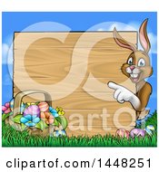 Poster, Art Print Of Cartoon Happy Brown Easter Bunny Rabbit Pointing Around A Wood Sign With A Basket And Eggs In Grass