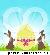 Clipart Of A Yellow Easter Egg With Chocolate Bunnies Against A Sunrise Royalty Free Vector Illustration