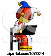 Yellow Jester Joker Man Using Laptop Computer While Sitting In Chair Angled Right