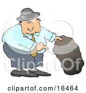 Caucasian Man In A Black Hat Blue Shirt Slacks And Gray Shoes Holding Up A Rock And Pointing Underneath It