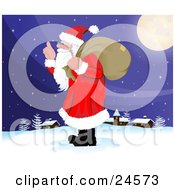 Santa Claus With A Long White Beard Carrying A Sack Over His Shoulder And Walking In The Snow Near A Quiet Village On Christmas Eve