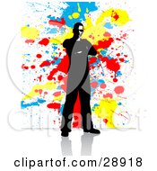 Poster, Art Print Of Black Mostly Silhouetted Man Standing With His Arms Crossed On A Reflective White Surface With A Background Of Blue Yellow And Red Paint Splatters