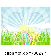 Clipart Illustration Of Three Colorful Easter Eggs In Spring Grass Under A Beautiful Morning Sunrise With Rays Of Light In The Blue Sky by elaineitalia