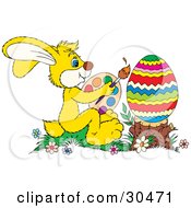 Poster, Art Print Of Cute Yellow Bunny Rabbit Sitting In Flowers Holding A Palette And Paint Brush And Painting A Large Easter Egg Propped On A Stump