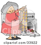 Gray Haired Woman Holding Up A Clean Towel In Front Of A Washer And Dryer While Doing Laundry