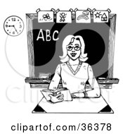 Poster, Art Print Of Friendly Female Teacher Reading A Book At Her Desk In A Class Room