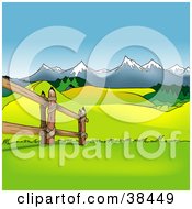 Wooden Fence Along A Green Pasture With Hills And Snow Capped Mountains
