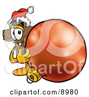 Clipart Picture Of A Wooden Cross Mascot Cartoon Character Wearing A Santa Hat Standing With A Christmas Bauble by Toons4Biz