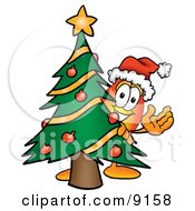 Flame Mascot Cartoon Character Waving And Standing By A Decorated Christmas Tree